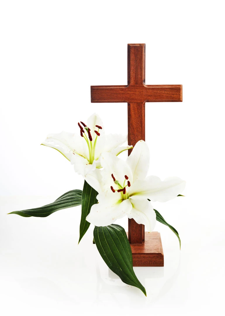 Wooden cross with white lilies and green leaves on a clean white background for sympathy.