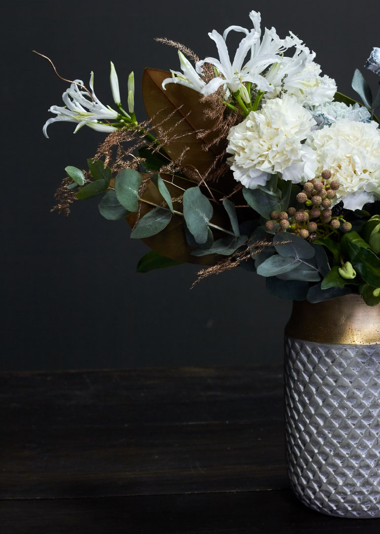 White flowers and greenery arranged in a silver textured vase on dark background