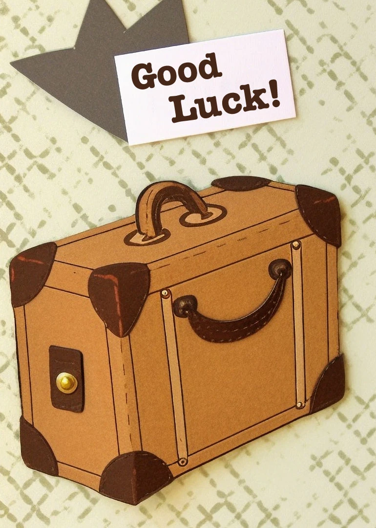 A suitcase illustration with Good Luck text on a patterned background and dark corner details.