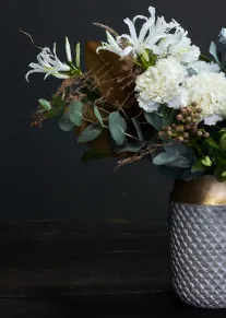 White floral bouquet with eucalyptus and dried grasses arranged in a textured gold and silver vase.
